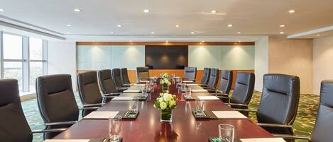 A conference room with a long table, black chairs, and a floral centerpiece.