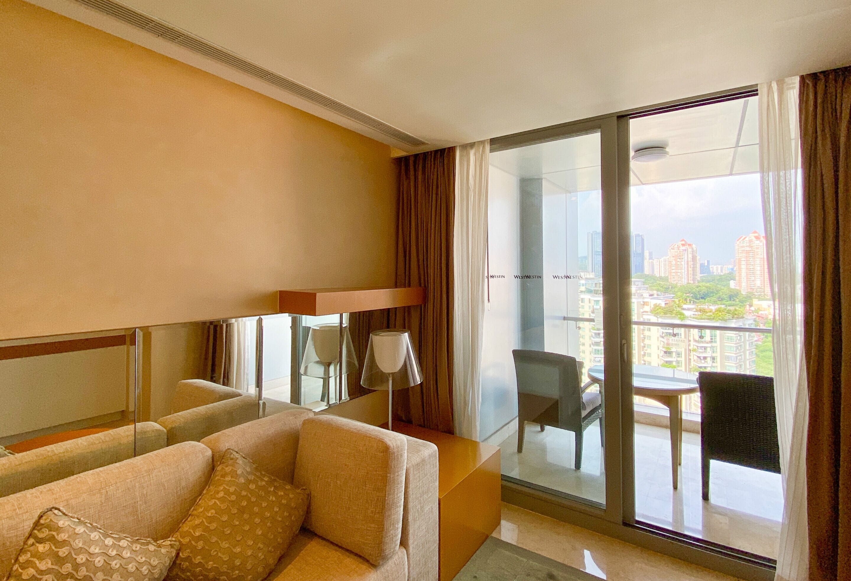 A hotel room with a sofa, a small table, and a balcony with a view of the city.
