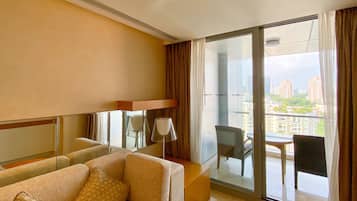 A hotel room with a sofa, a small table, and a balcony with a view of the city.
