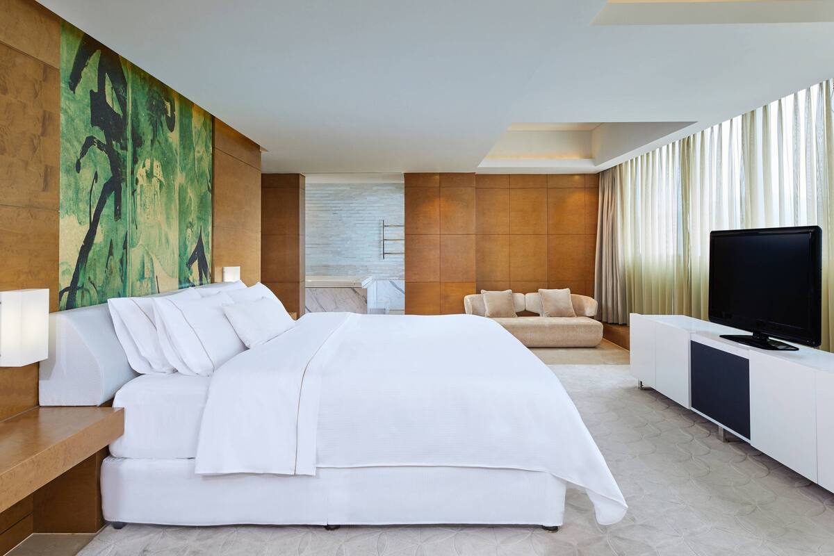 A modern hotel room with a large bed, a television, and a seating area with a sofa.