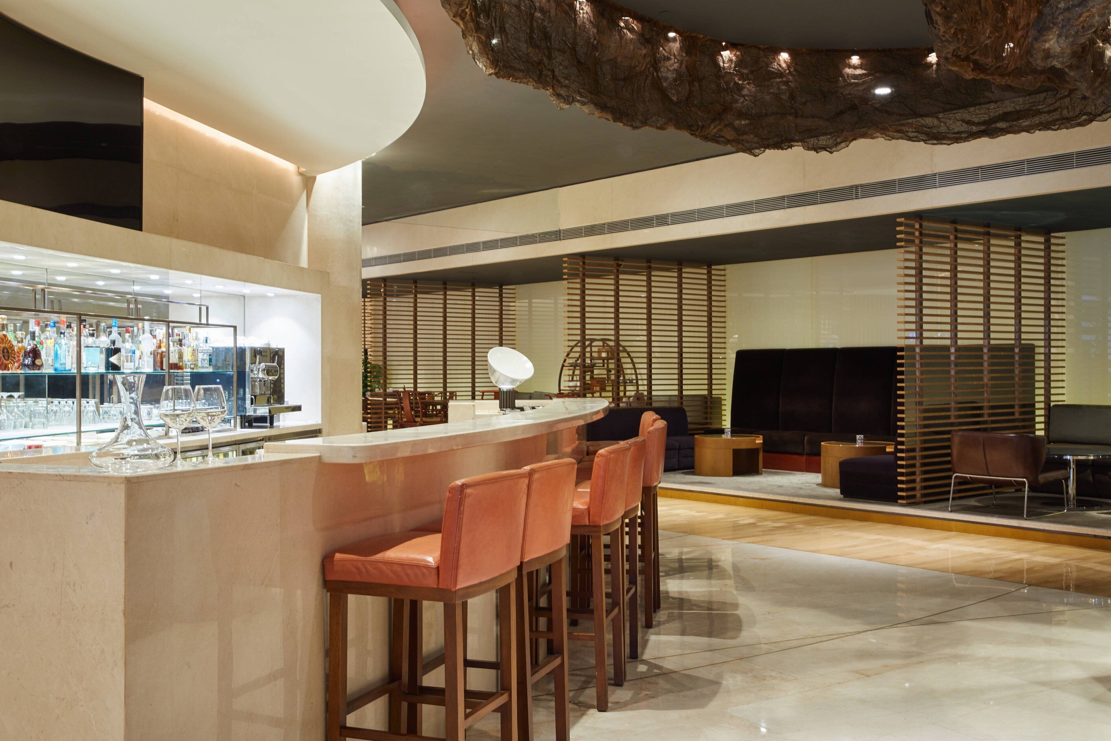 A modern bar area with a counter, bar stools, and a seating area with a sofa and chairs.