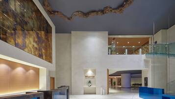 Un moderno vestíbulo de hotel con un mostrador de recepción, el logotipo de Westin y una escalera de cristal.