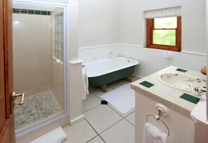 Een badkamer met een douche met glazen wand, een vrijstaand bad en een wastafel met een raam erboven.