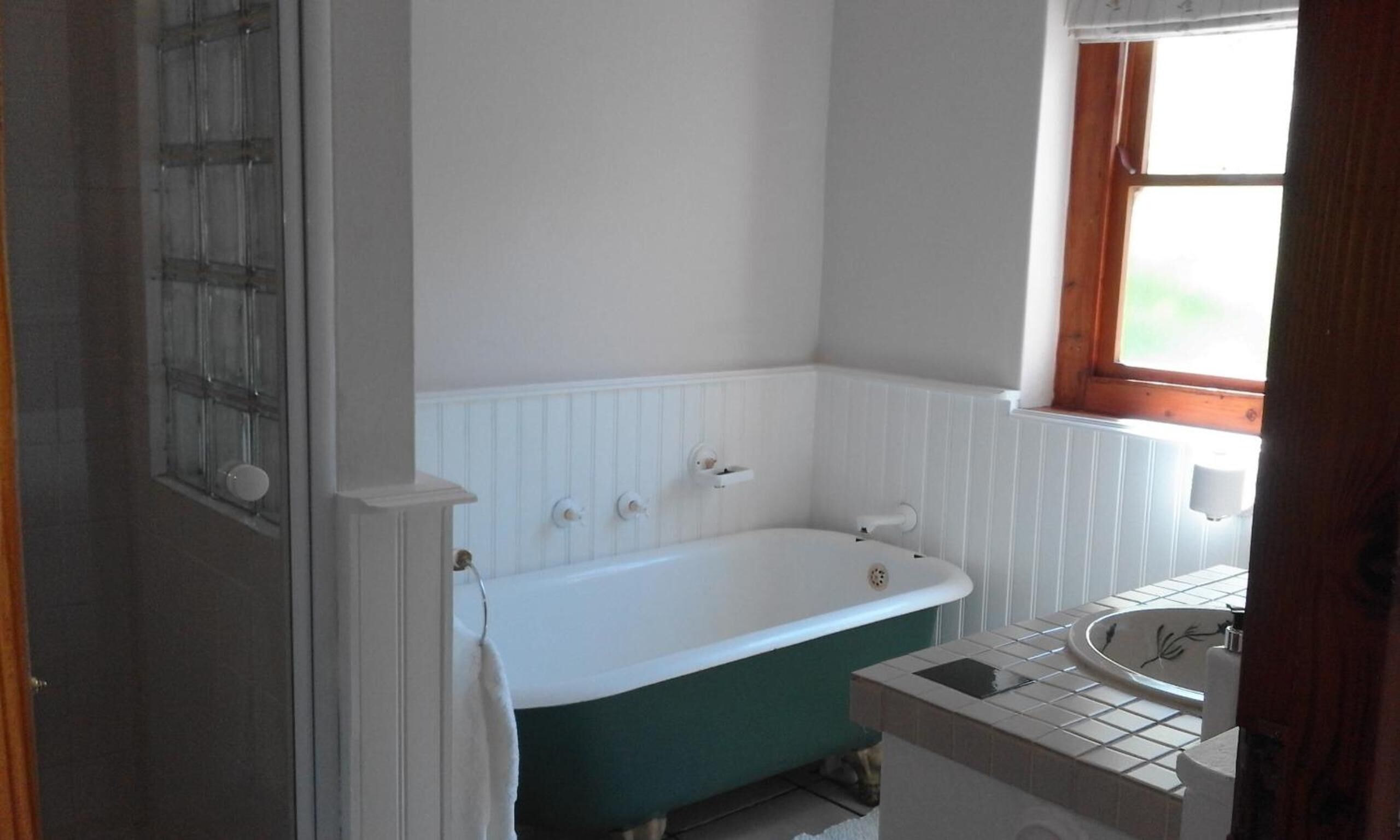 Baño con una bañera blanca, ventana y lavamanos con azulejos.