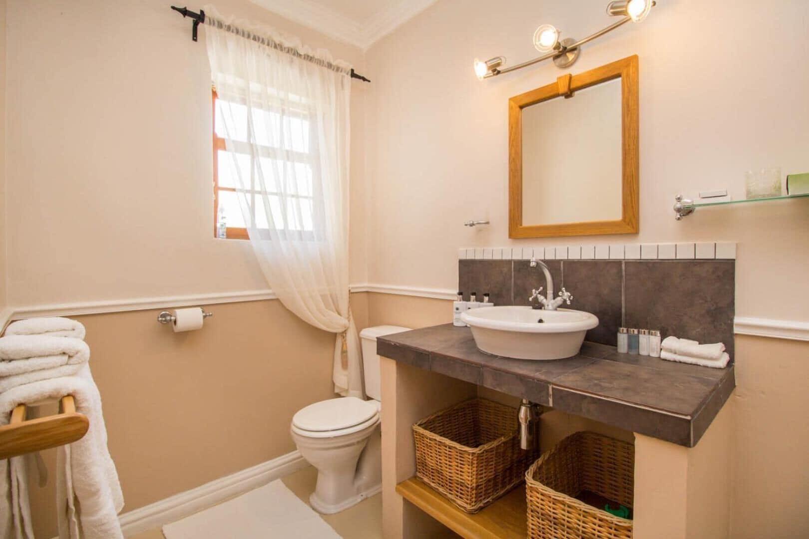 A bathroom with a toilet, sink, and a mirror. There are baskets under the sink and a towel rack to the left.