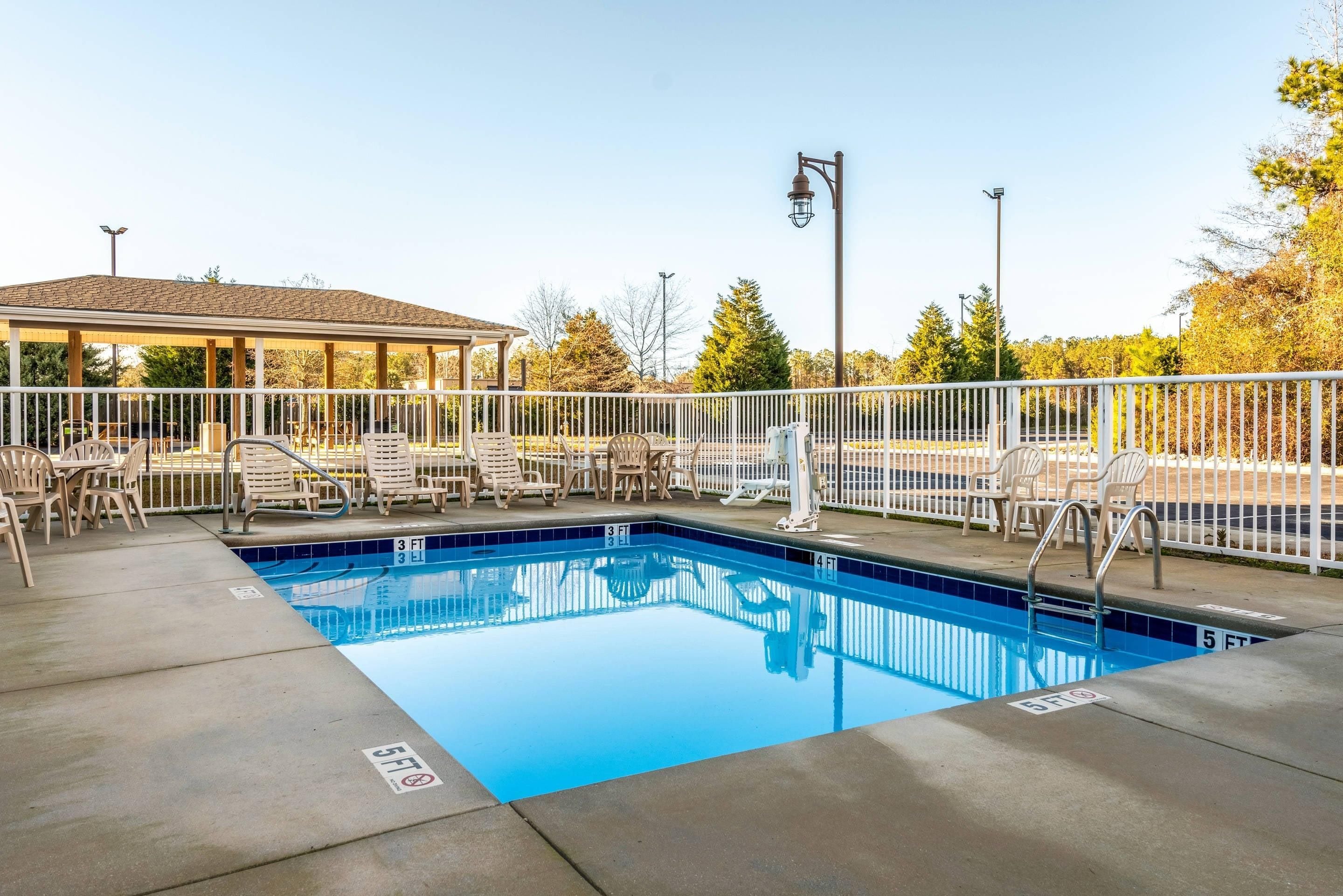 A rectangular swimming pool with a white deck area, surrounded by a white fence.