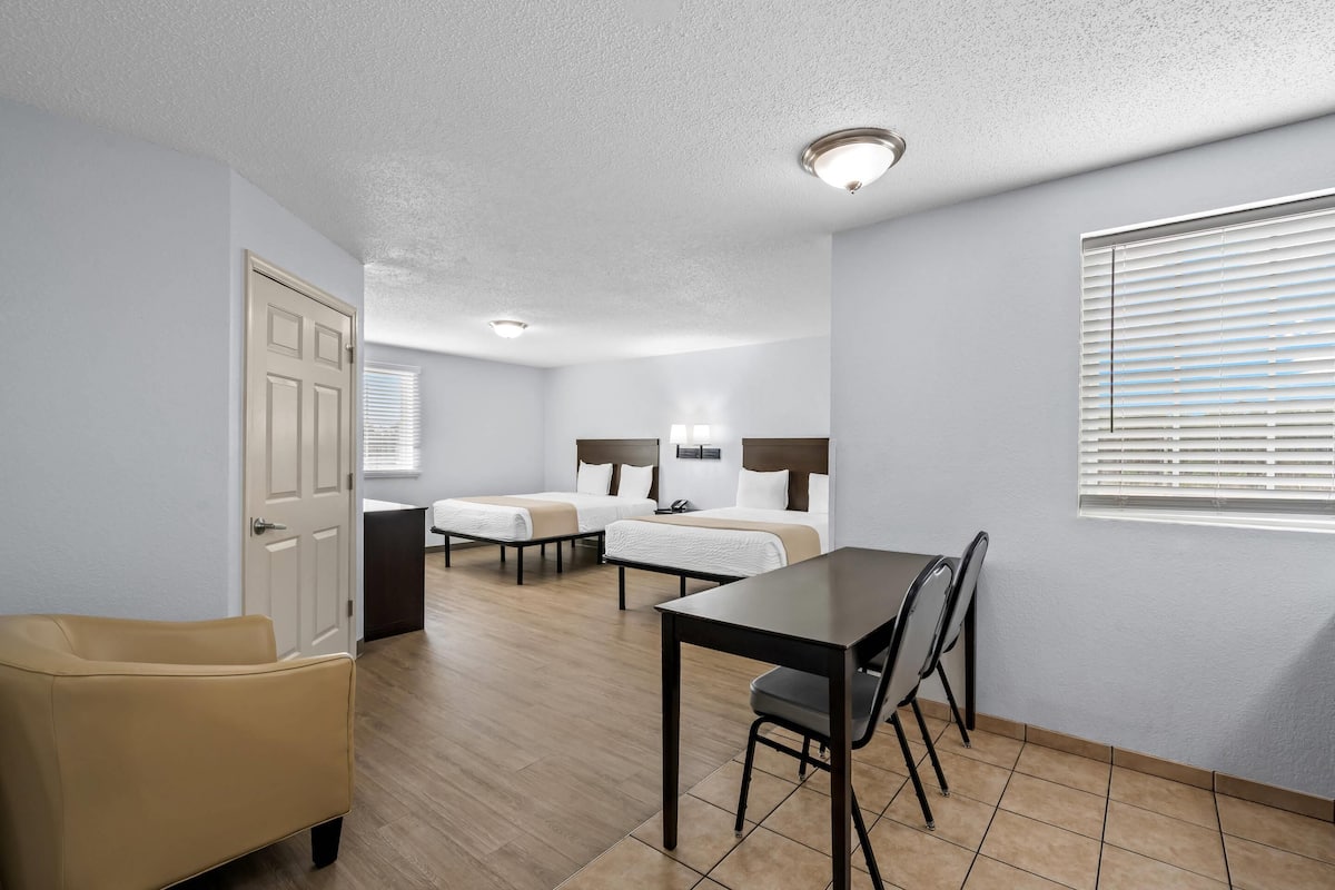 Une chambre d’hôtel avec deux lits simples, une table à manger avec des chaises, un canapé et une fenêtre avec des stores.
