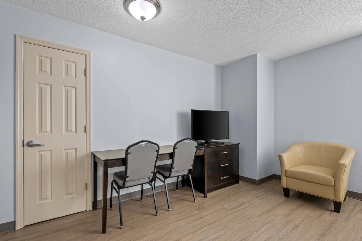 Une pièce comprenant un bureau, deux chaises, un téléviseur, un meuble et un fauteuil.