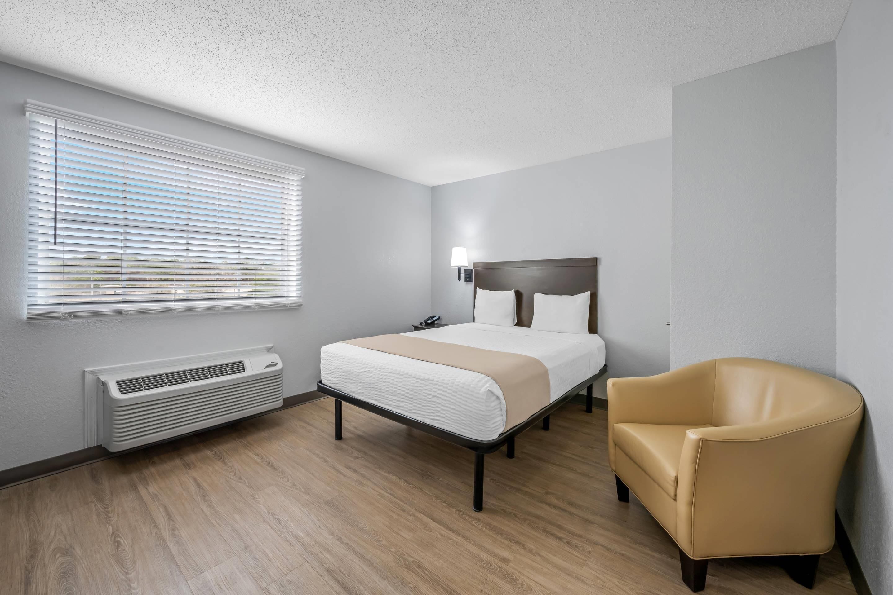 Une chambre d’hôtel avec un lit, une chaise, un radiateur et une fenêtre avec des stores.