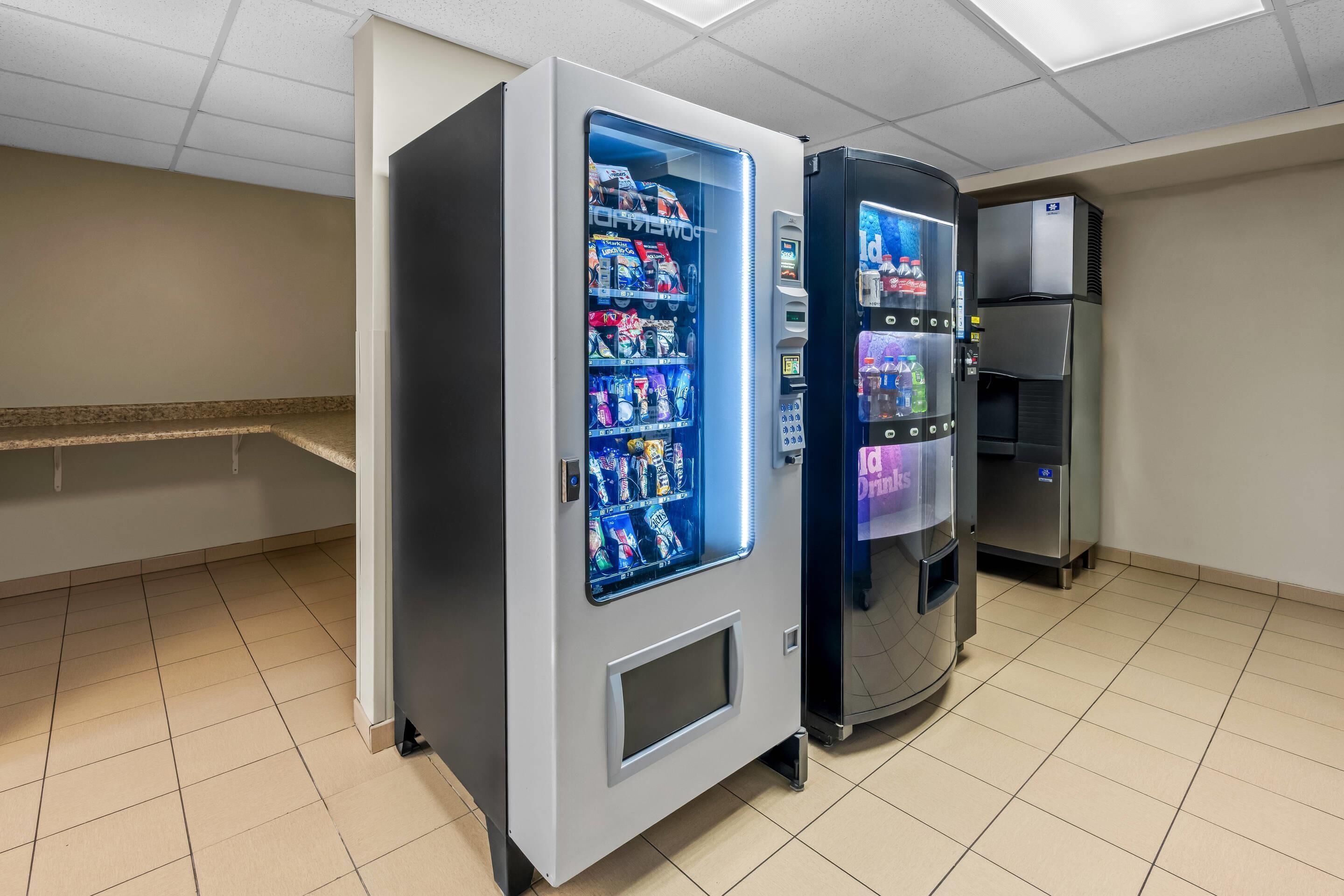 A vending machine area with two beverage dispensers and a refrigerated unit in a clean, tiled room.