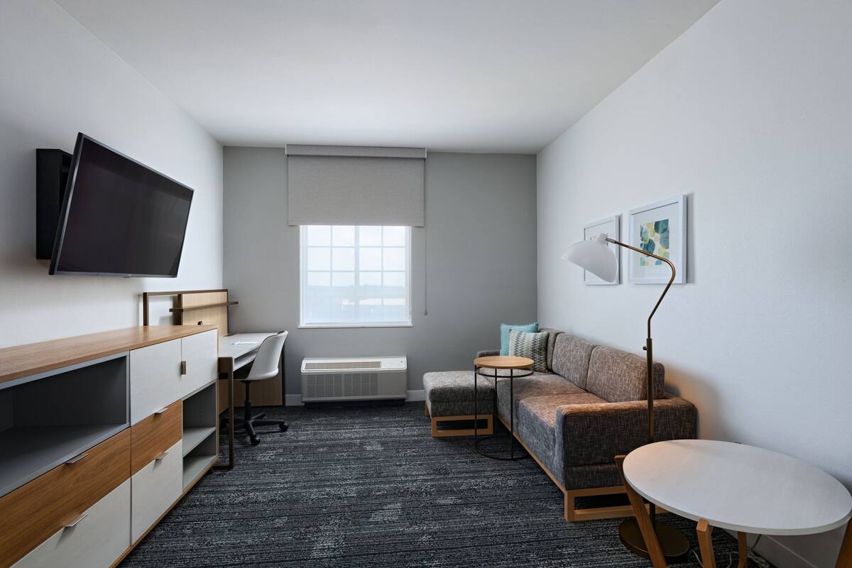 A modern, compact room with a flat-screen TV, a desk, a sofa, a small round table, and a standing lamp.