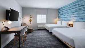 Una camera d'albergo con una scrivania, due letti, una televisione e un'ampia finestra.