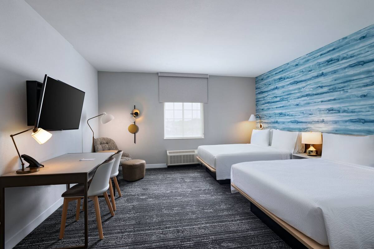 A hotel room with a desk, two beds, a TV, and a large window.