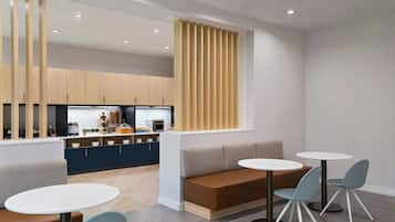 Un comedor moderno con cocina al fondo, que presenta una distribución con asientos tipo banca y mesas redondas.