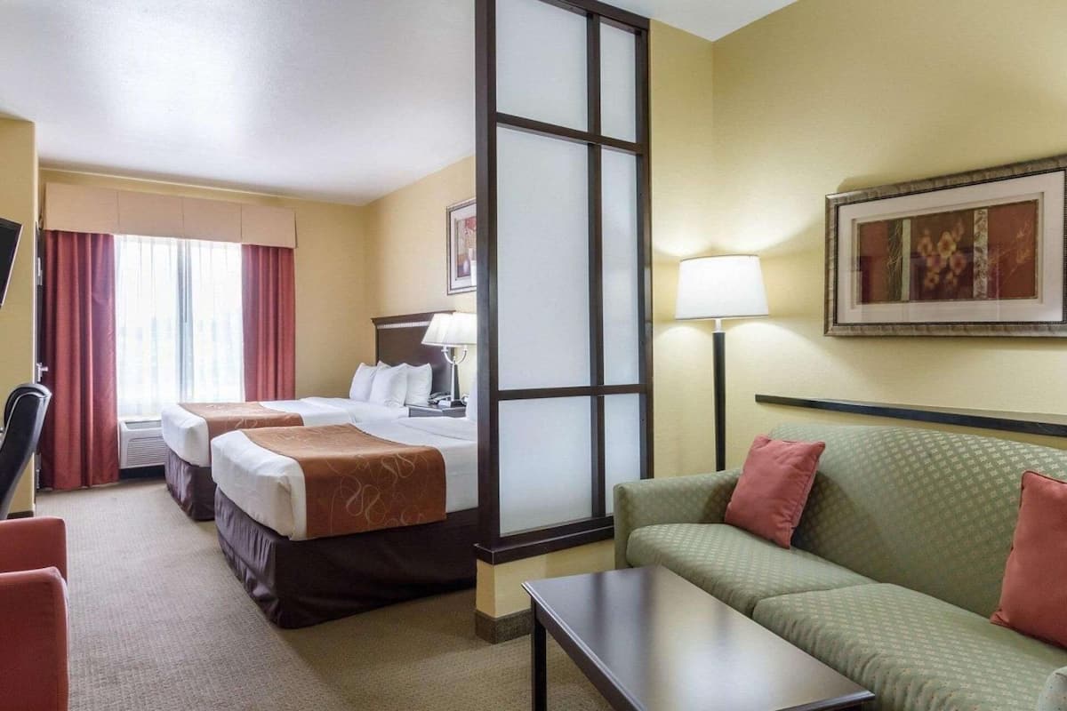 A hotel room with two beds, a sofa, a table, a lamp, and a window with curtains.