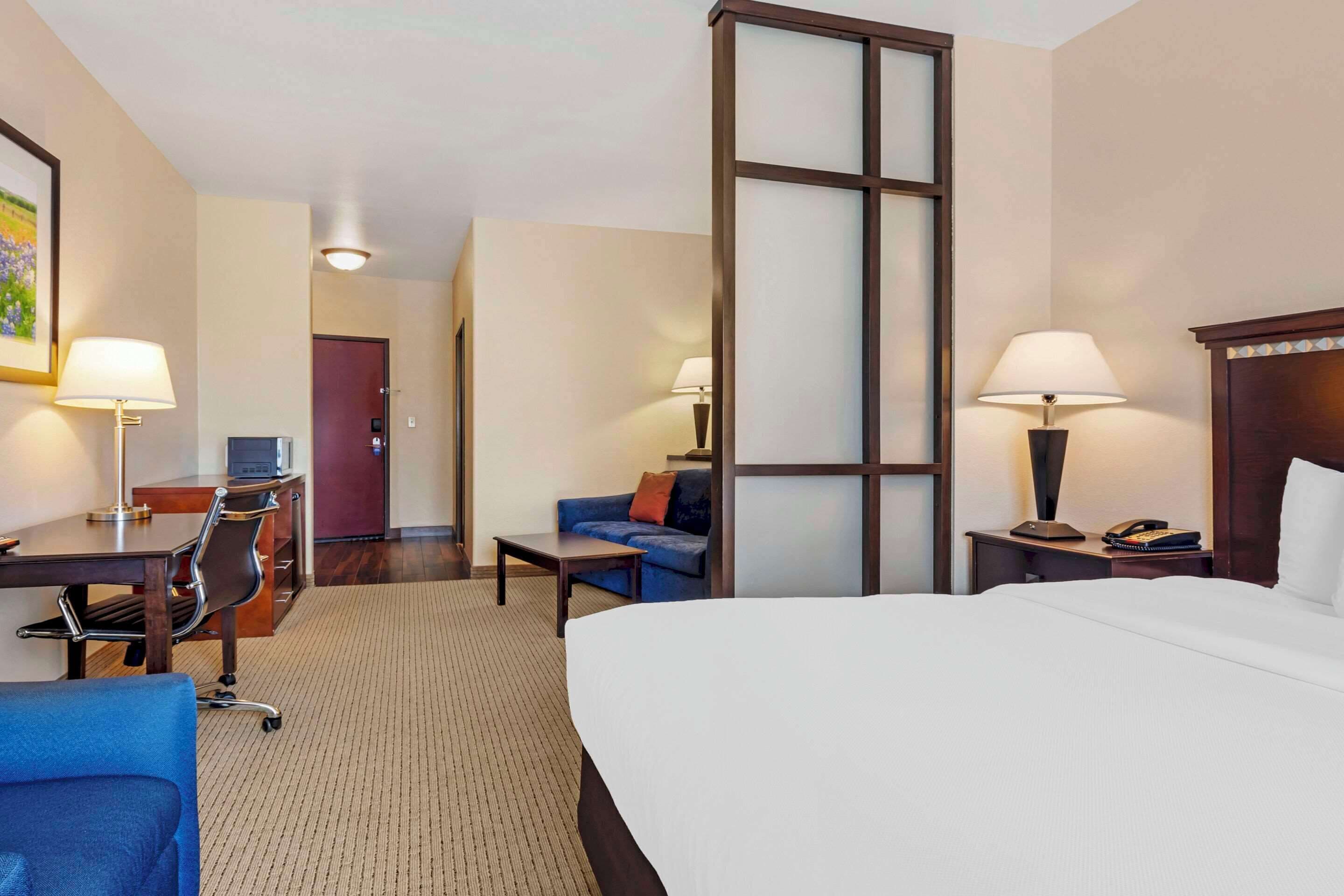 A hotel room with a large bed, a desk with a chair, a sofa, a small table, and a lamp.