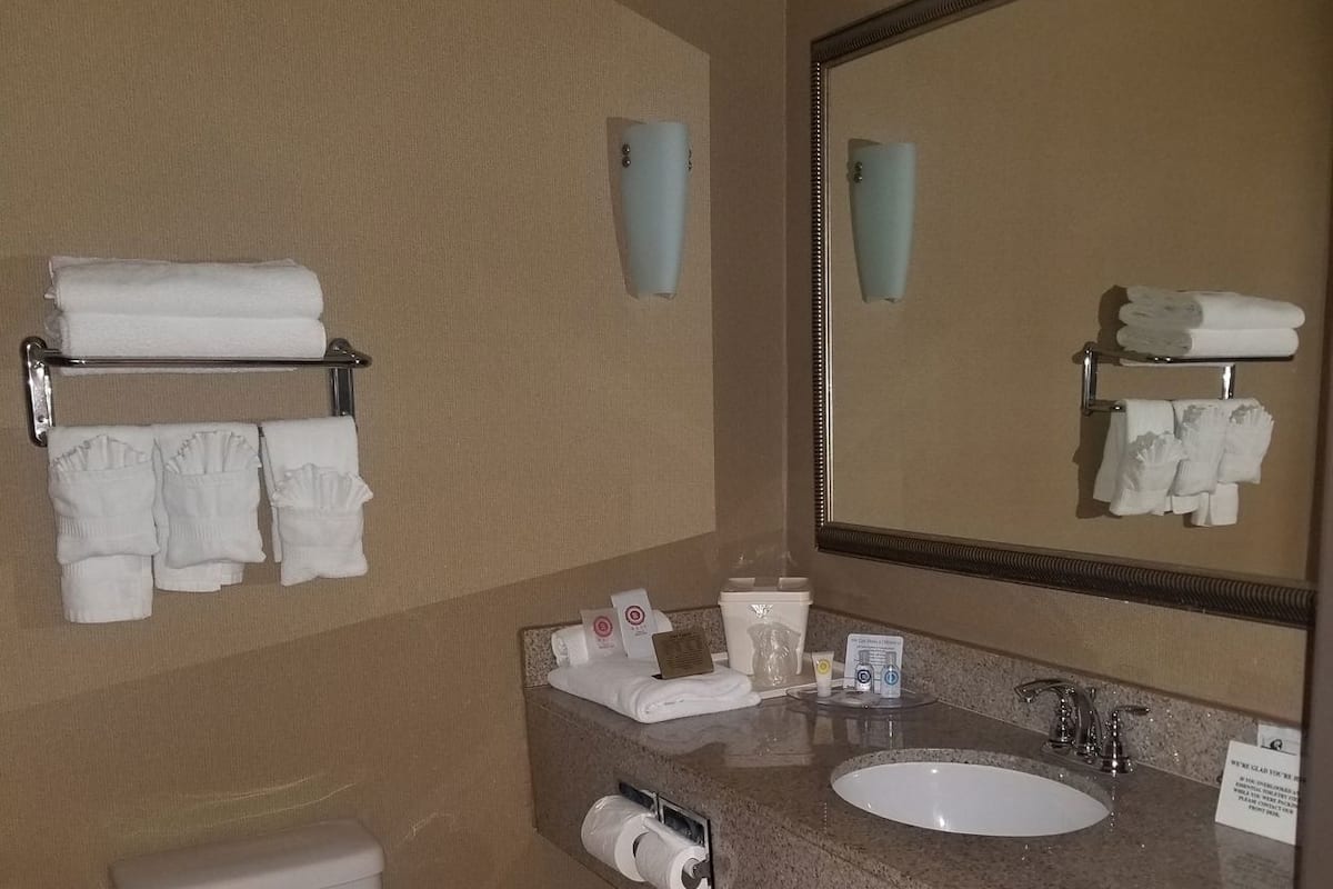 A bathroom with a toilet, sink, mirror, towel rack, and toiletries.