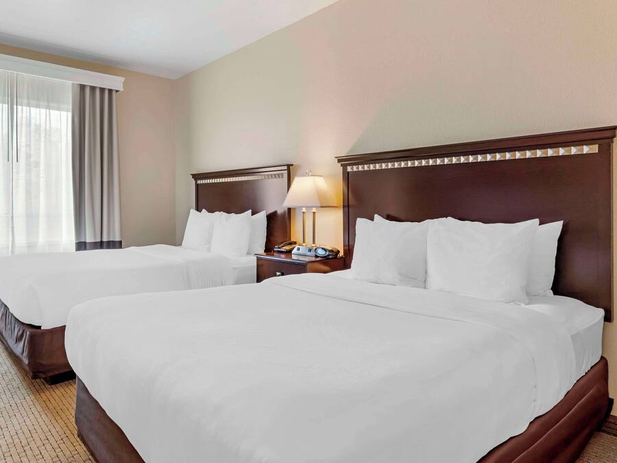A hotel room with two beds, a nightstand with a lamp, and a window with curtains.
