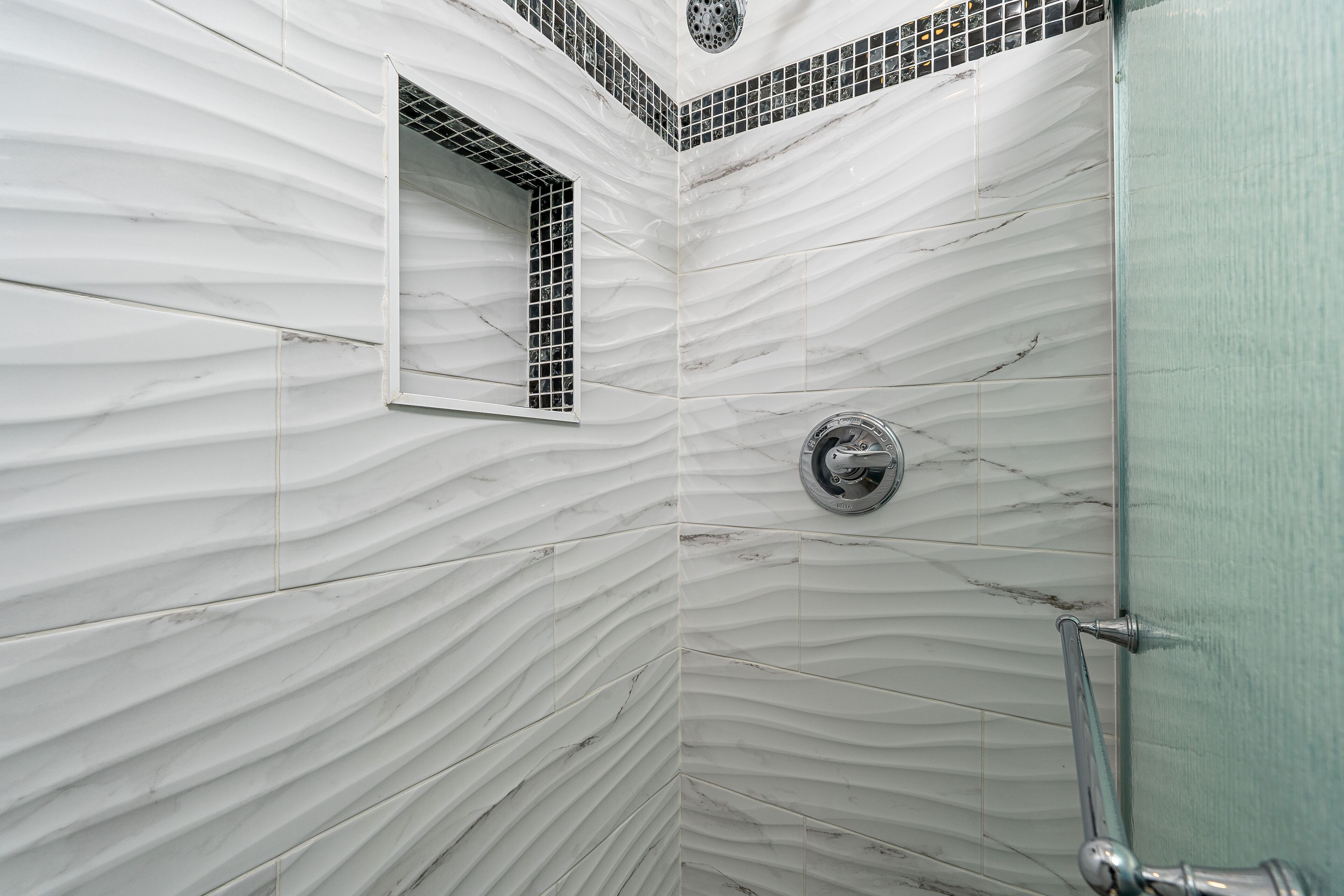 Eine Dusche mit Marmorwand, einem kleinen Fenster und einem Metall-Duschkopf.