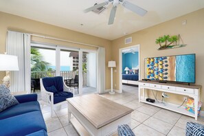 A living room with a TV, sofa, coffee table, and a balcony with a view of the ocean.