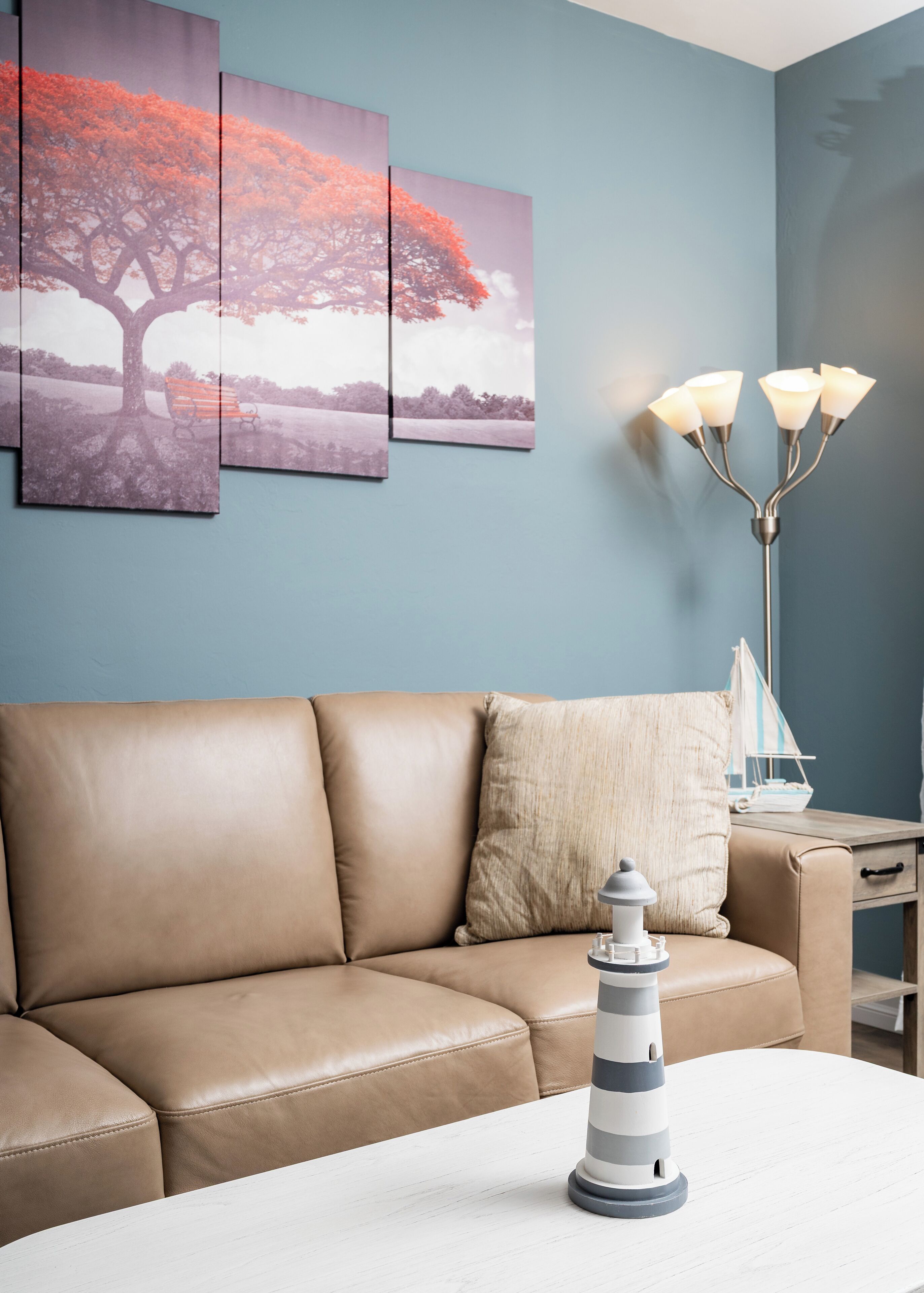 Ein modernes Wohnzimmer mit einem beigefarbenen Ledersofa, einem weißen Couchtisch, einer dekorativen Leuchtturm-Figur und einer wandmontierten Stehlampe.