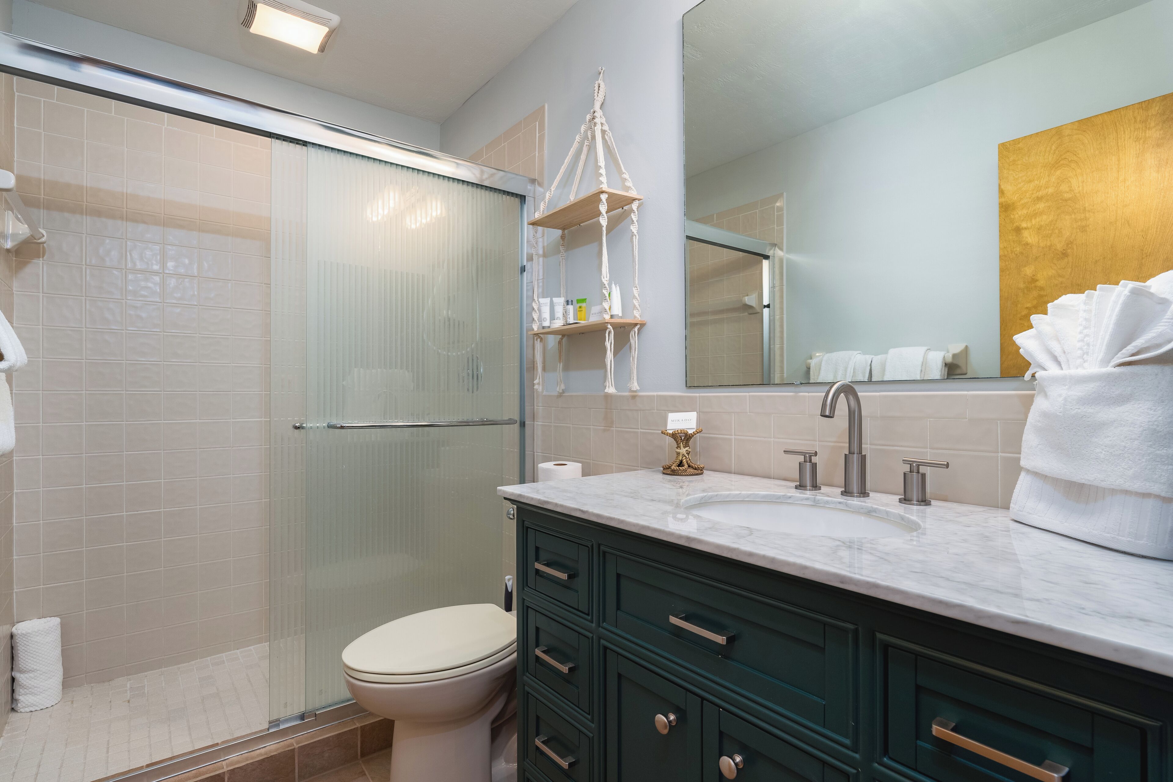 A modern bathroom with a glass shower enclosure, a white toilet, a marble sink, and dark green cabinets.