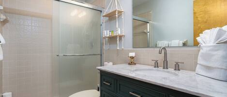Een moderne badkamer met een douchecabine van glas, een wit toilet, een marmeren wastafel en donkergroene kastjes.