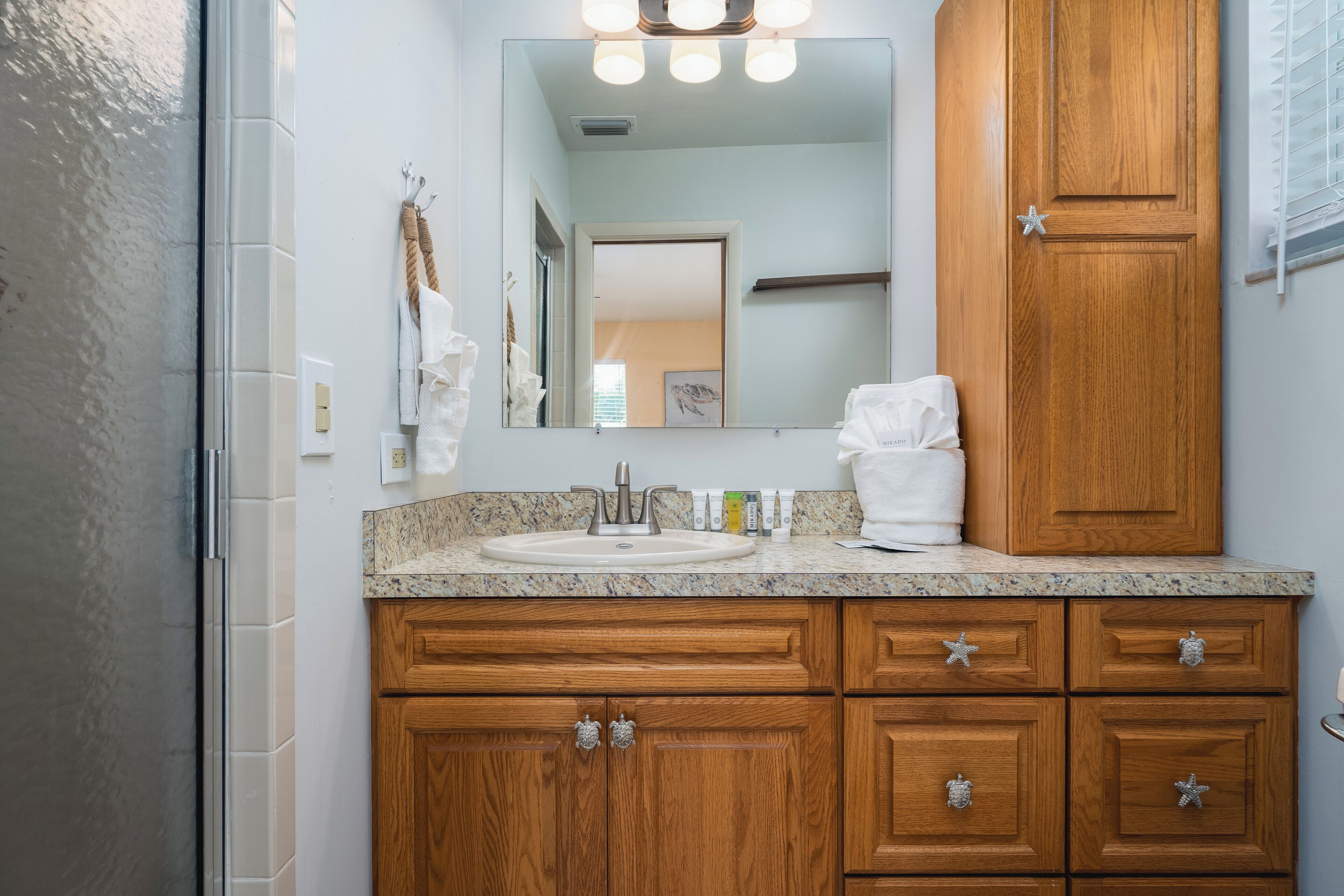 A bathroom with a granite countertop, wooden cabinets, a sink, and a mirror with lights.