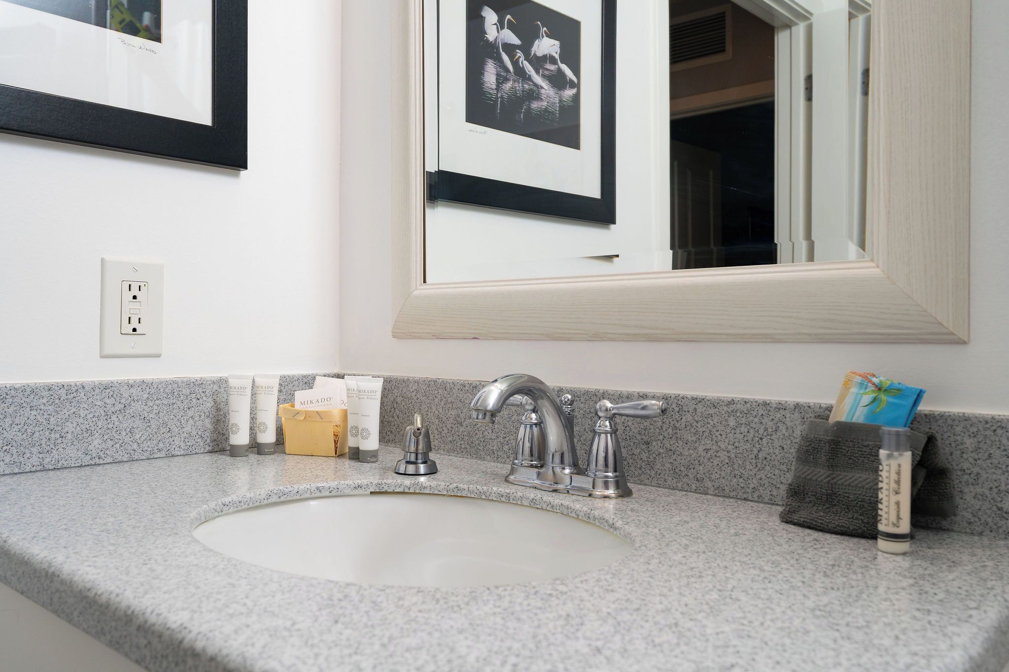 A bathroom with a granite countertop, a sink, a mirror, and a framed picture on the wall.