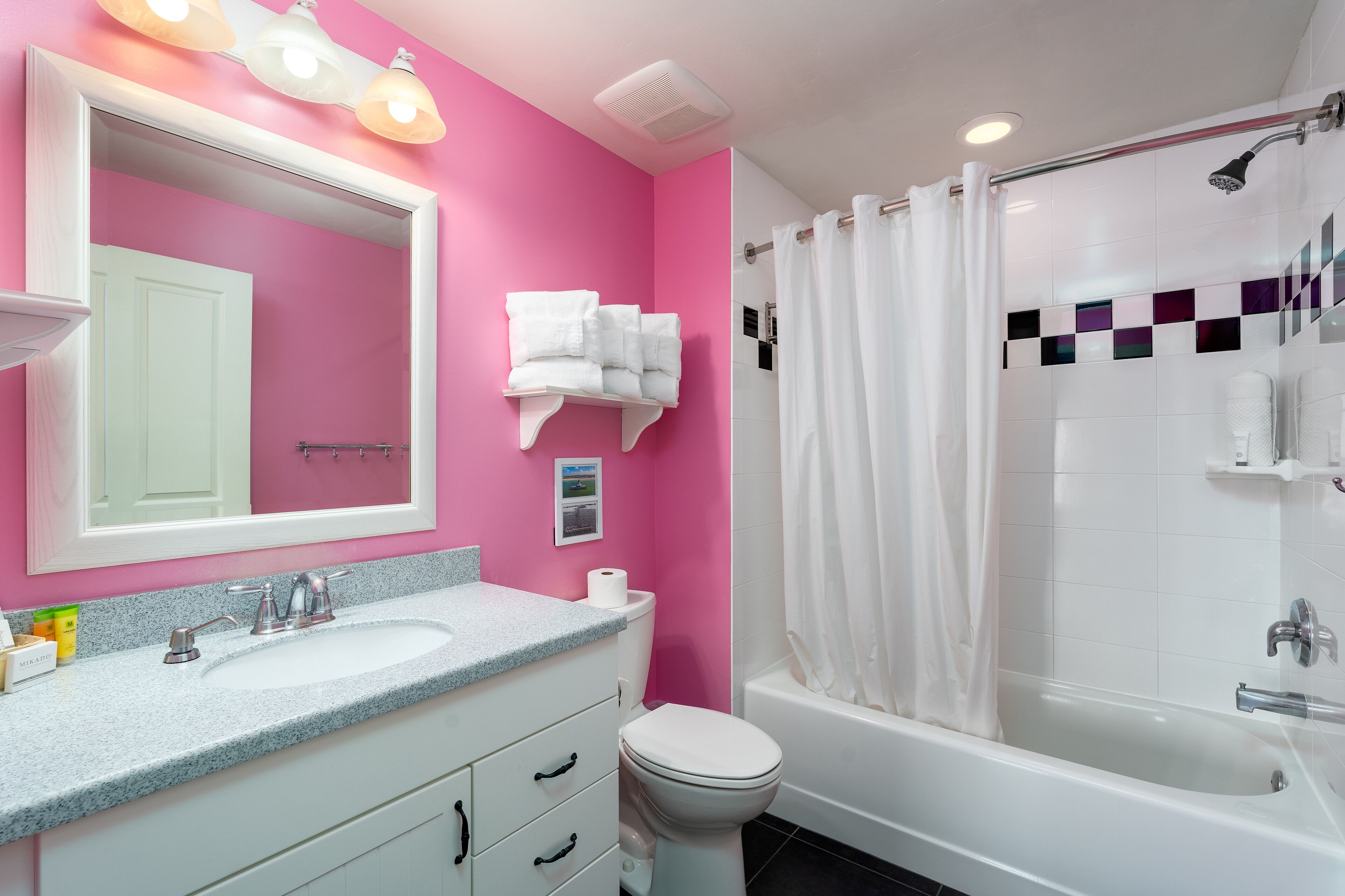 A bathroom with a pink wall, a white sink, a toilet, and a bathtub with a shower curtain.