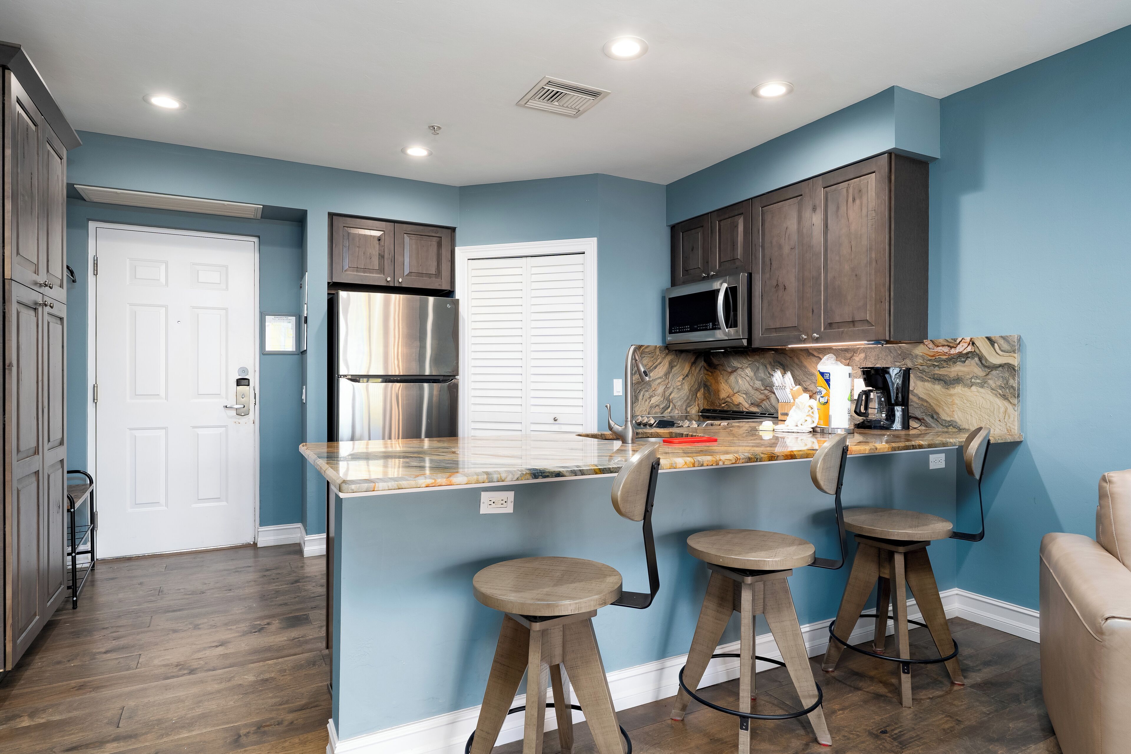 A kitchen with a central island, bar stools, a microwave, and a stainless steel refrigerator.