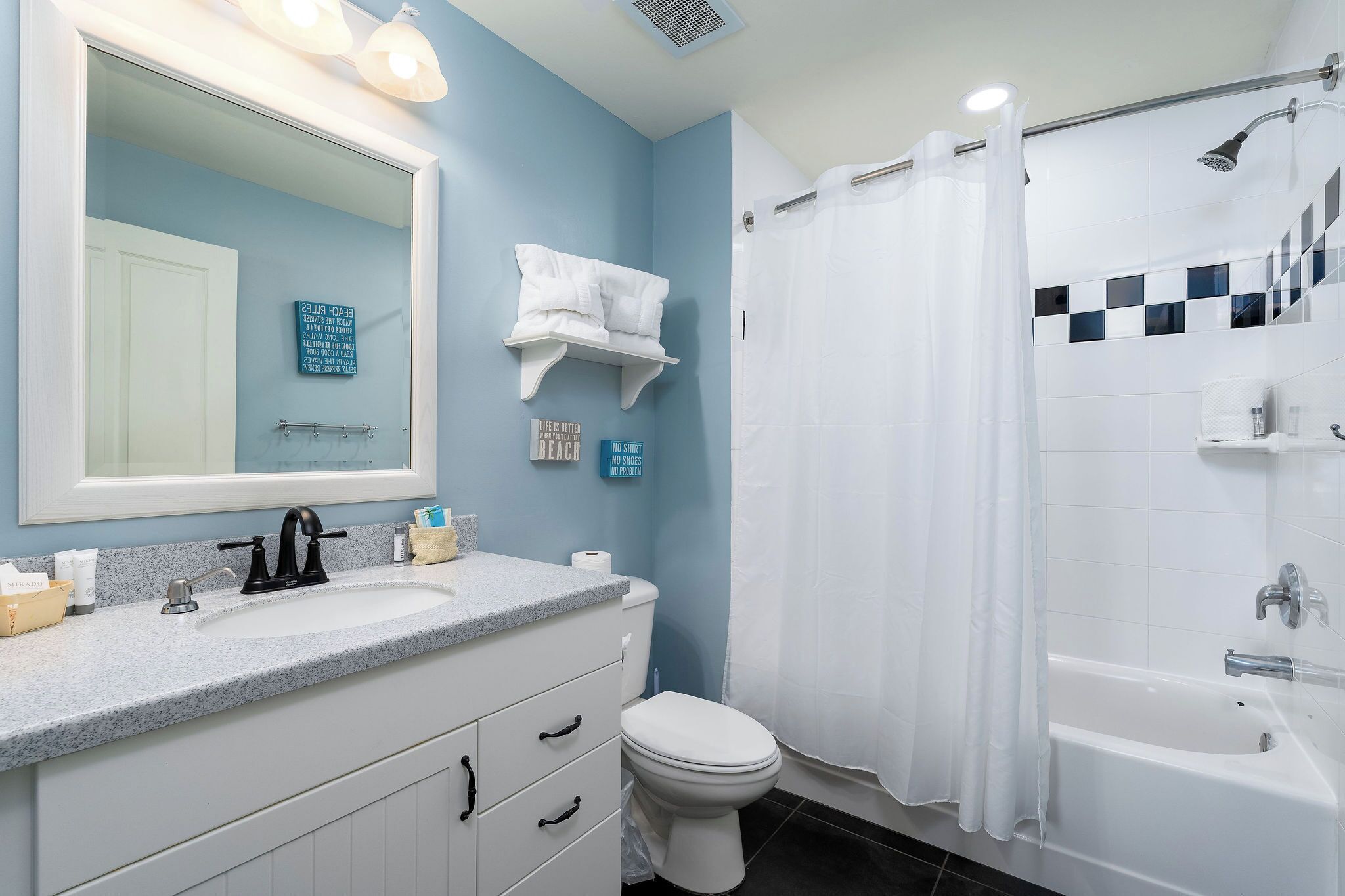 A bathroom with a white sink, a large mirror, a toilet, and a bathtub with a shower curtain.