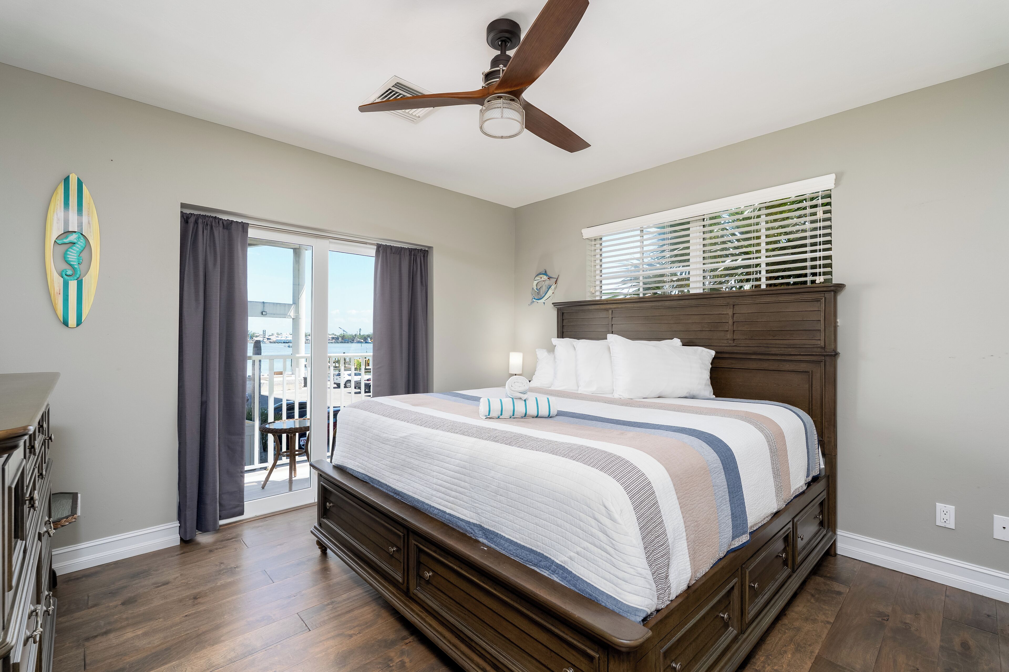Un dormitorio con una cama grande, un ventilador de techo, una ventana con persianas y vistas al exterior.