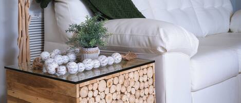 A white sofa with a green throw blanket, a wooden side table with a plant, and a wall with palm tree murals.