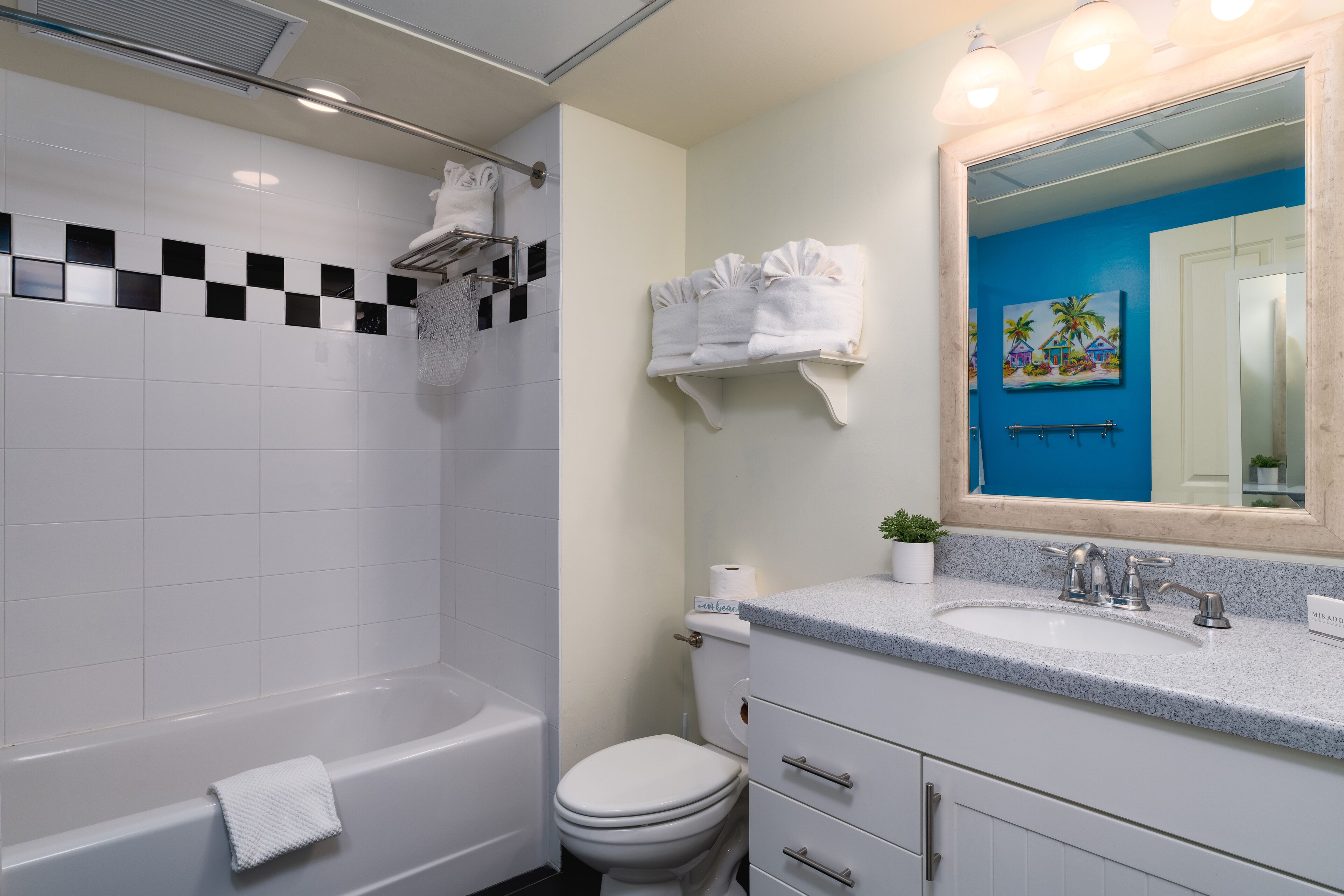 A bathroom with a bathtub, toilet, sink, and a mirror with a blue wall.