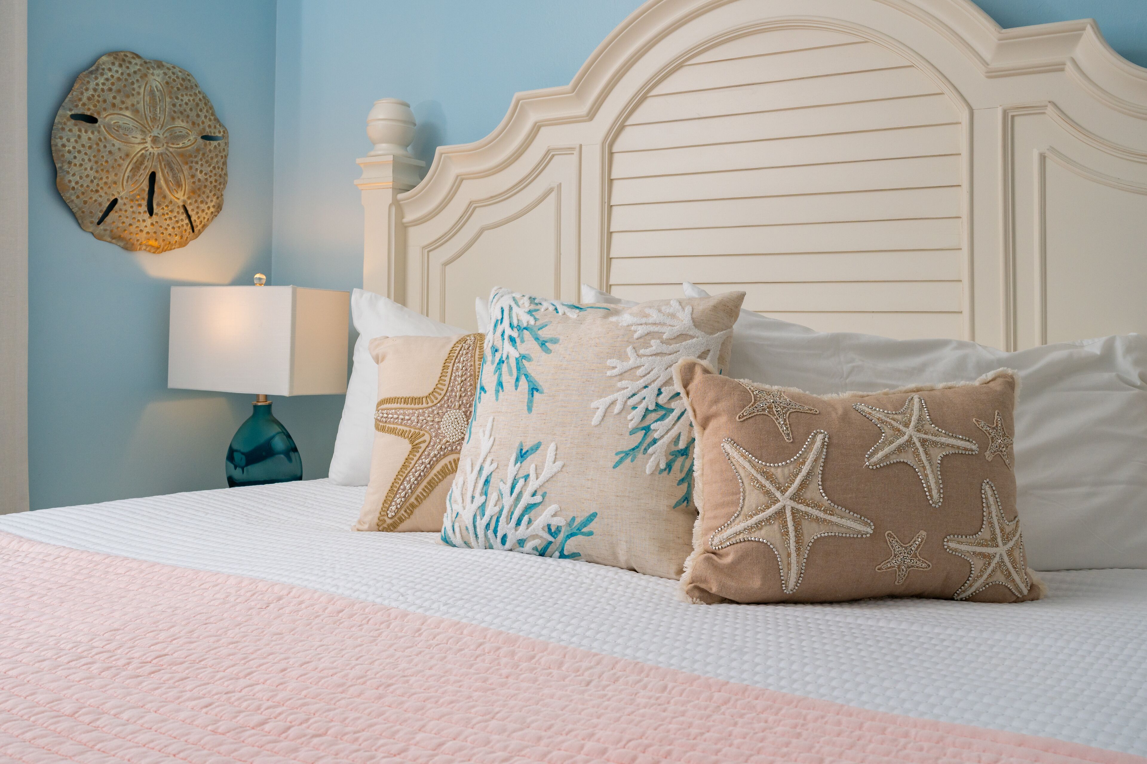 A bed with a white headboard, a blue wall, and a decorative shell on the wall.