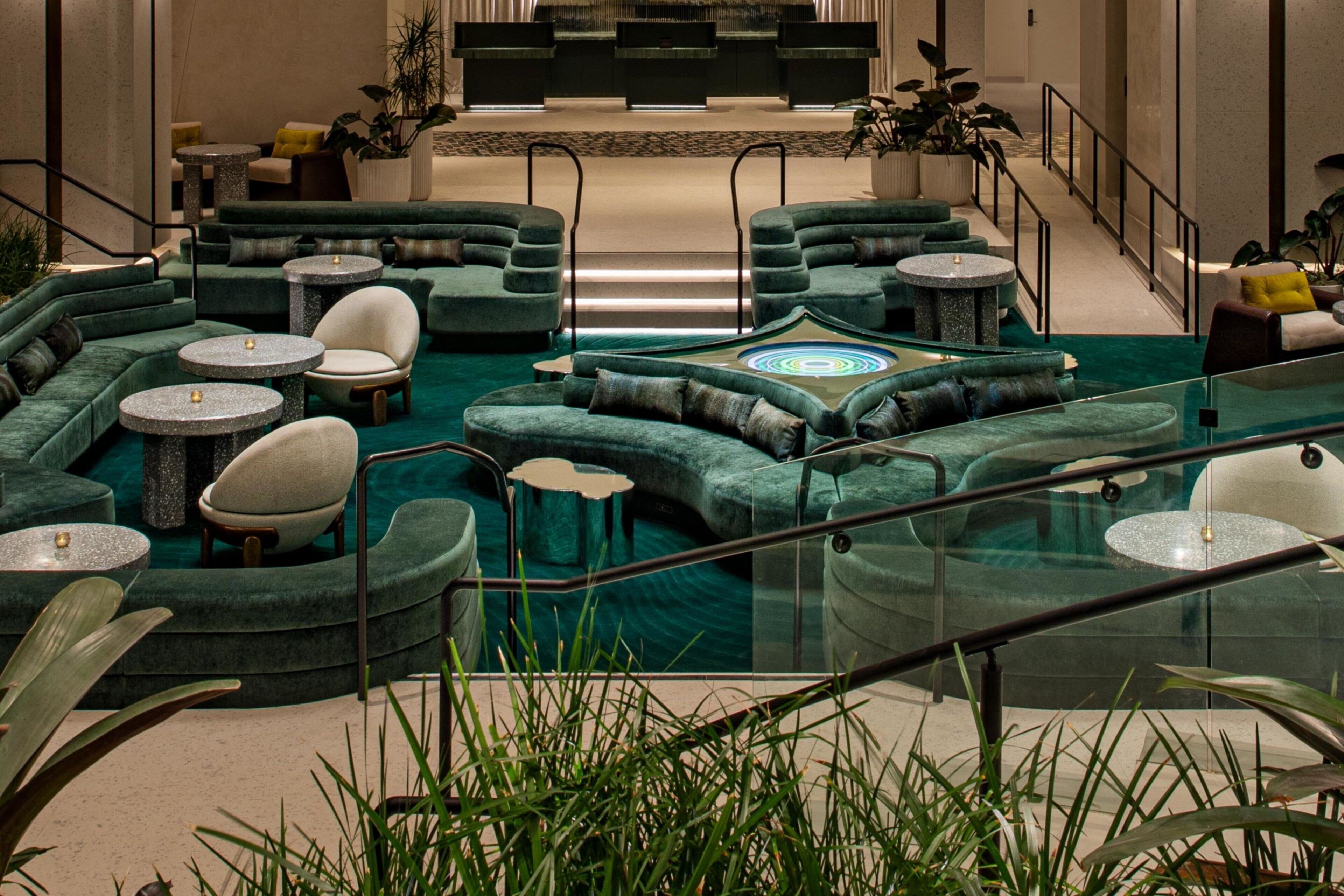 A modern lobby with green sofas, round tables, and a central water feature.