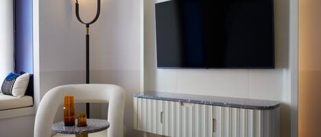 A modern living room with a white sofa, a round table with two candles, a floor lamp, and a mounted TV.