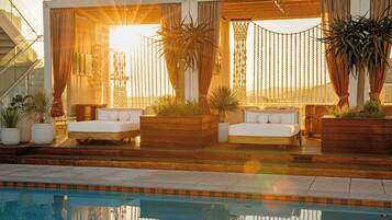 A poolside area with two white sofas, wooden planters with plants, and a glass railing.