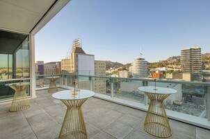 A rooftop terrace with glass tables and chairs, offering a city view.