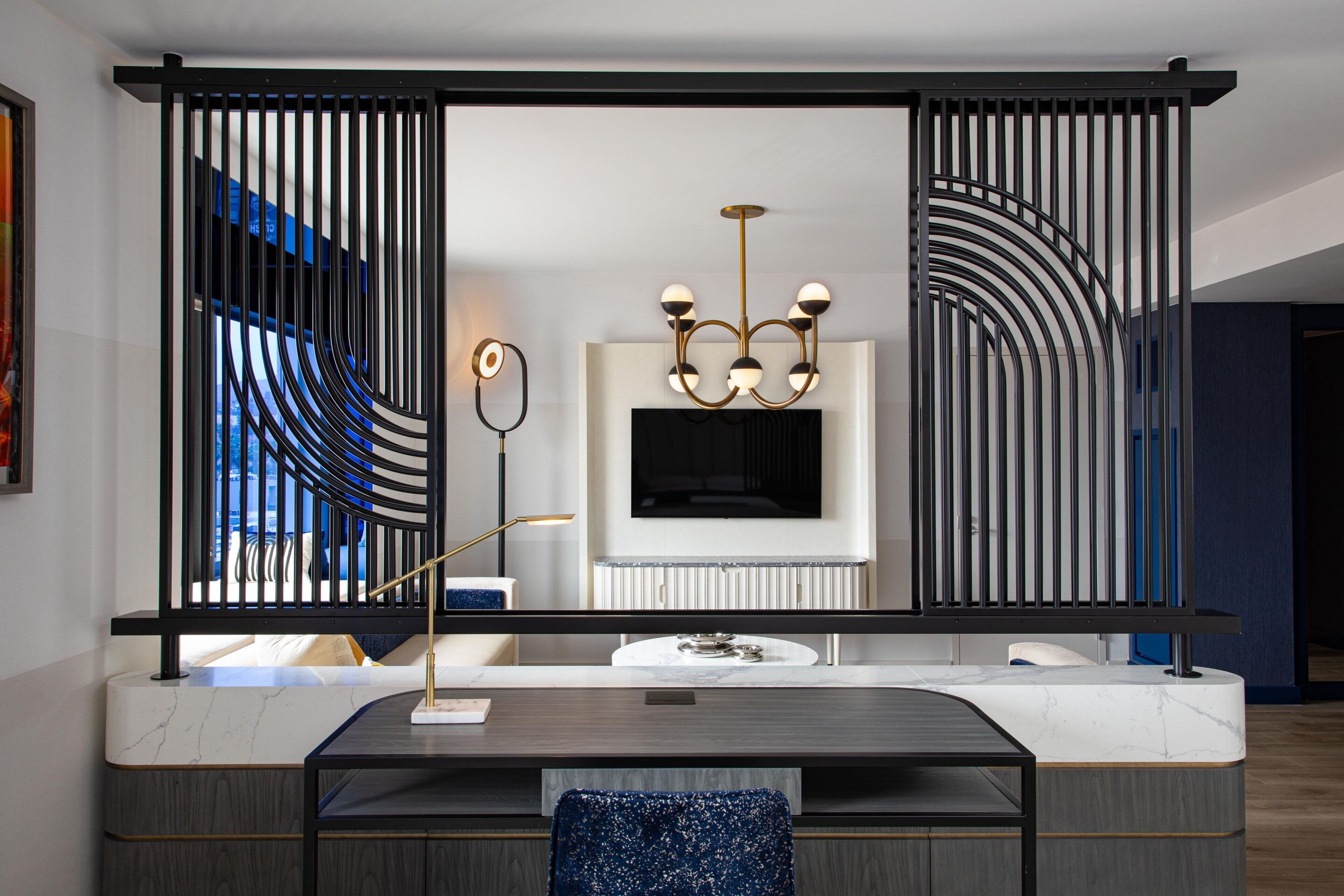 Un salon moderne avec une cheminée en marbre, un lustre noir et doré, et une cloison en métal noir.