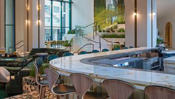A modern indoor space with a central bar area, seating arrangements, and a staircase leading to an upper level.