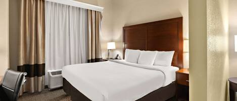 Habitación de hotel con una cama grande, un escritorio, una silla, una lámpara y una ventana con cortinas.