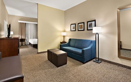 A hotel room with a blue sofa, a small ottoman, a desk with a lamp, a bed, and a large mirror.