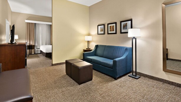 Habitación de hotel con un sofá azul, un pequeño reposapiés, un escritorio con lámpara, una cama y un espejo grande.