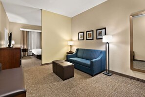 Ein Hotelzimmer mit einem blauen Sofa, einem kleinen Hocker, einem Schreibtisch mit Lampe, einem Bett und einem großen Spiegel.