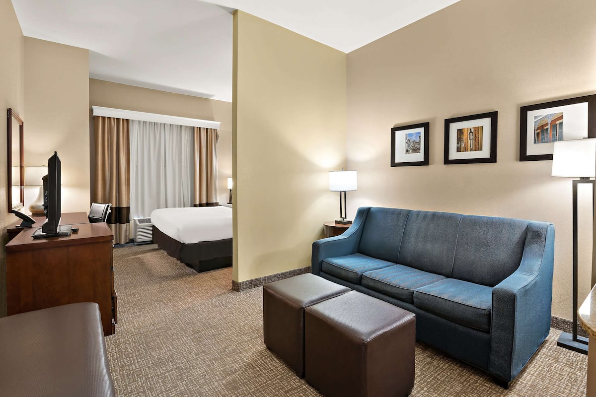 Una habitación de hotel con cama, sofá azul, escritorio con lámpara y cuadros en la pared.