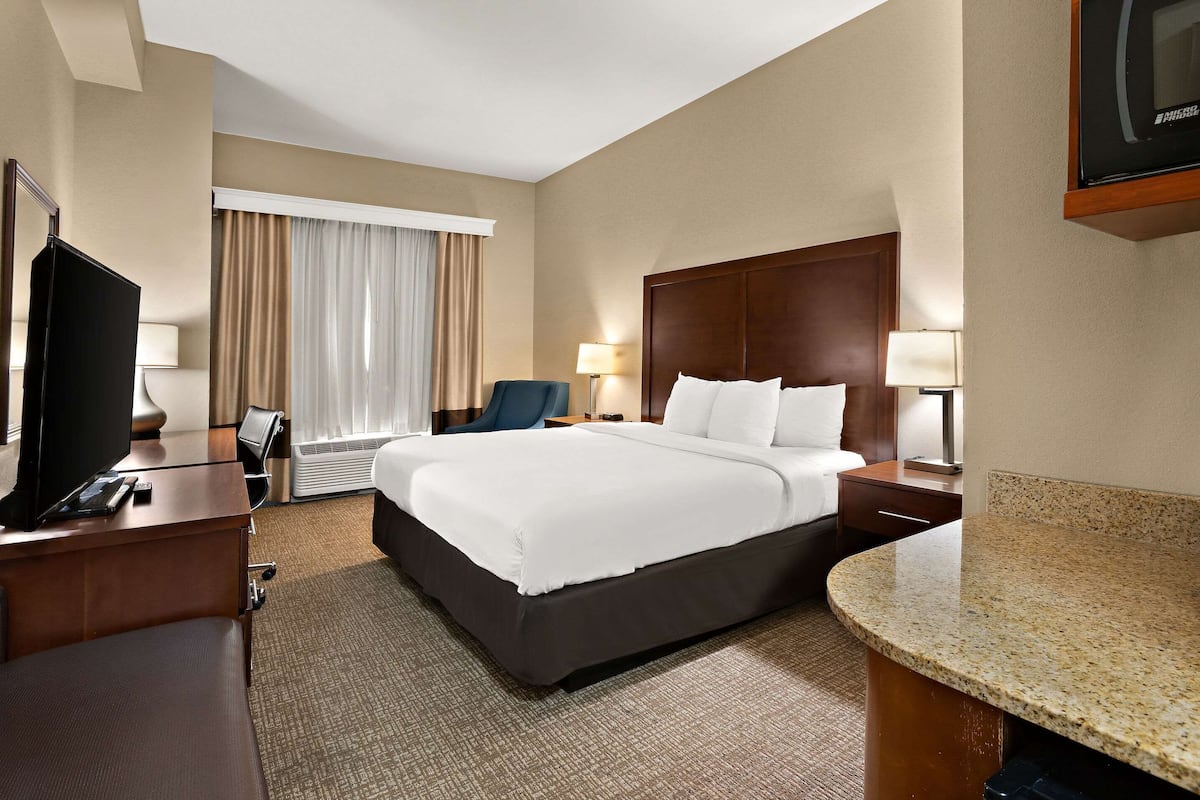 Una habitación de hotel con una cama grande, un escritorio con televisión, una silla y una mesita de noche con lámparas.