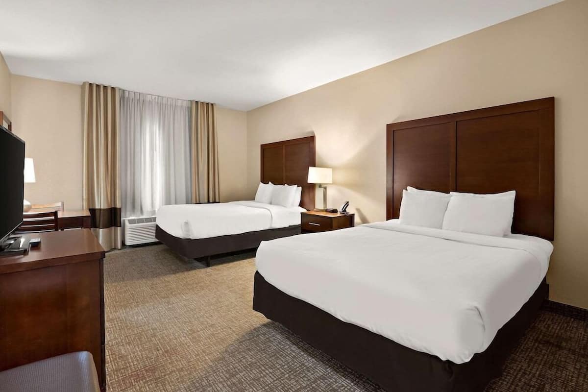 Habitación de hotel con dos camas, un escritorio, un televisor y una ventana con cortinas.
