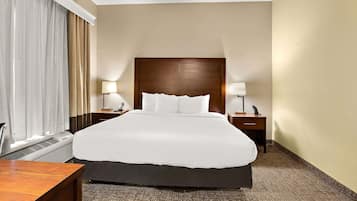 A hotel room with a large bed, two bedside tables with lamps, a desk, and a window with curtains.